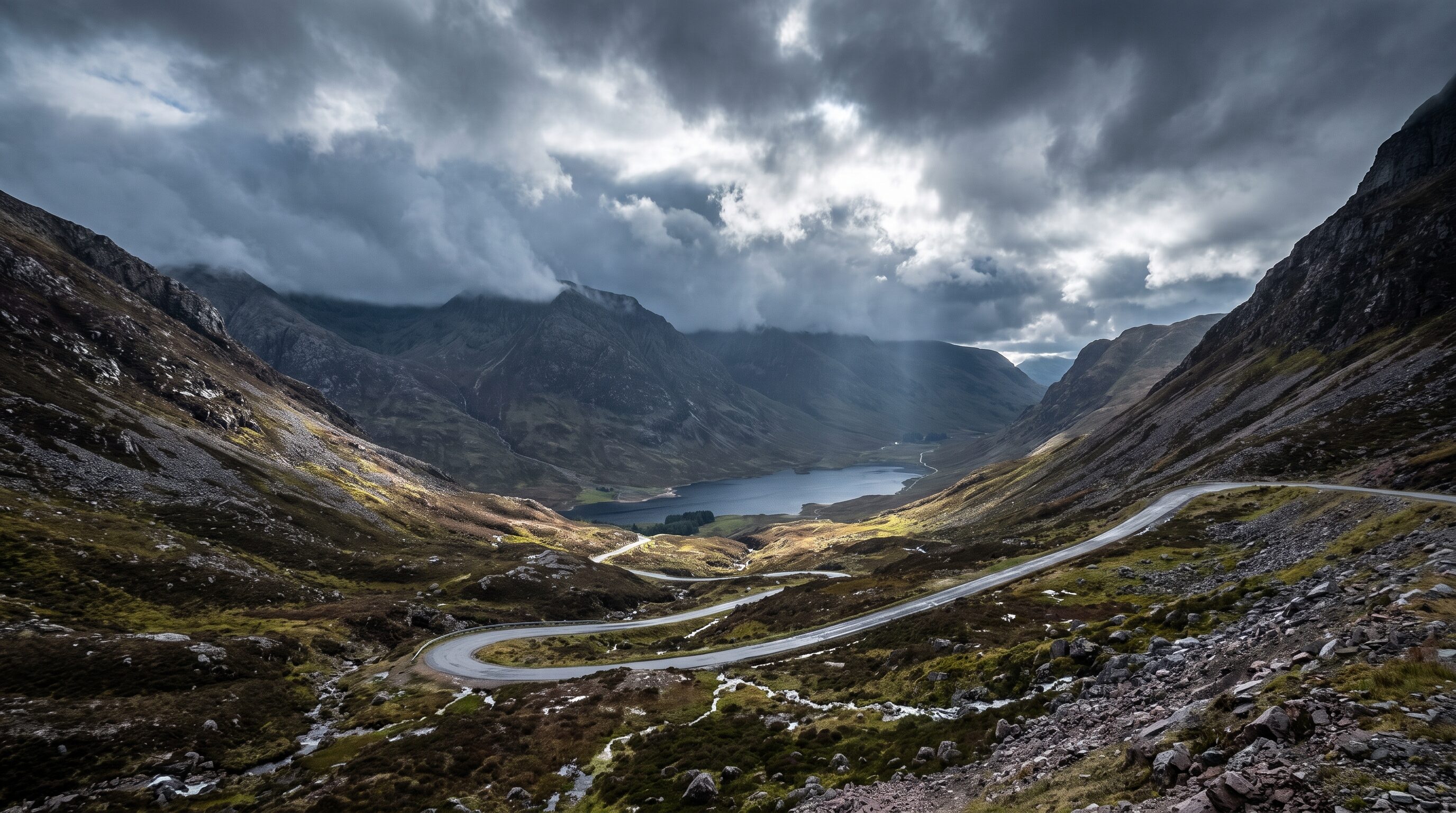 A single track mountain pass switchbacking up a bare rocky Highland glen under heavy cloud