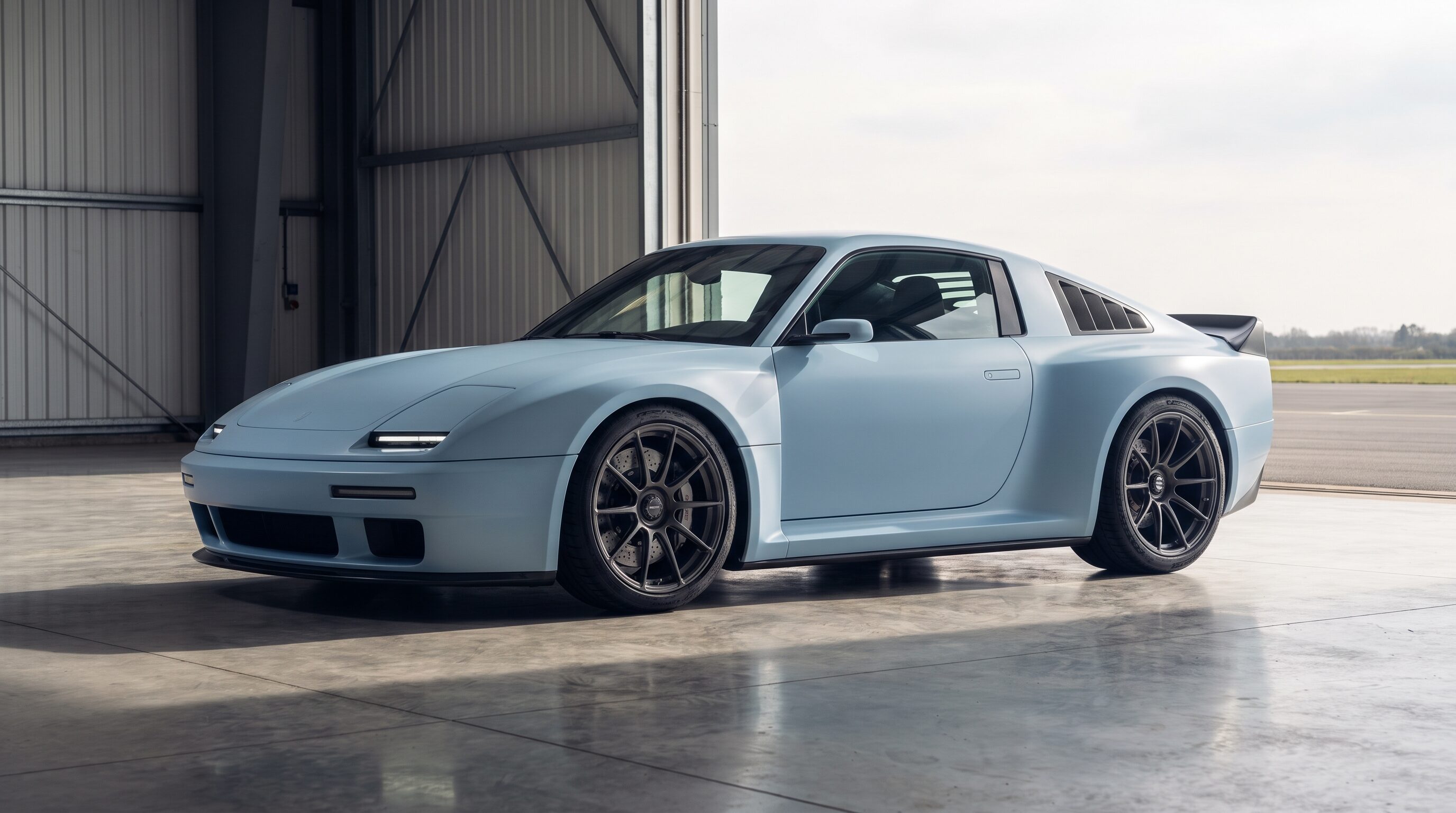 A pale ice blue rear engine sports coupe inside a bright aircraft hangar