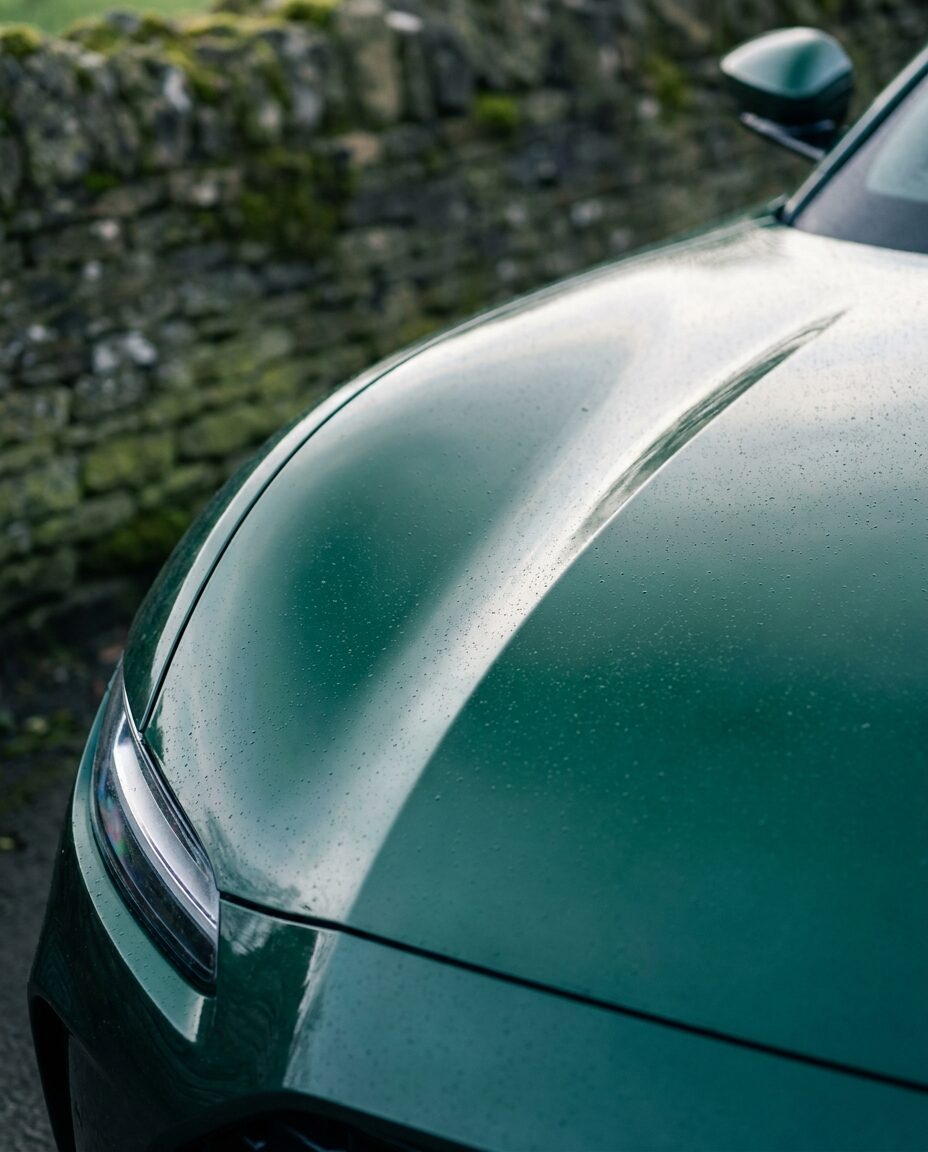 The long bonnet and front wing of a racing green grand tourer in soft daylight