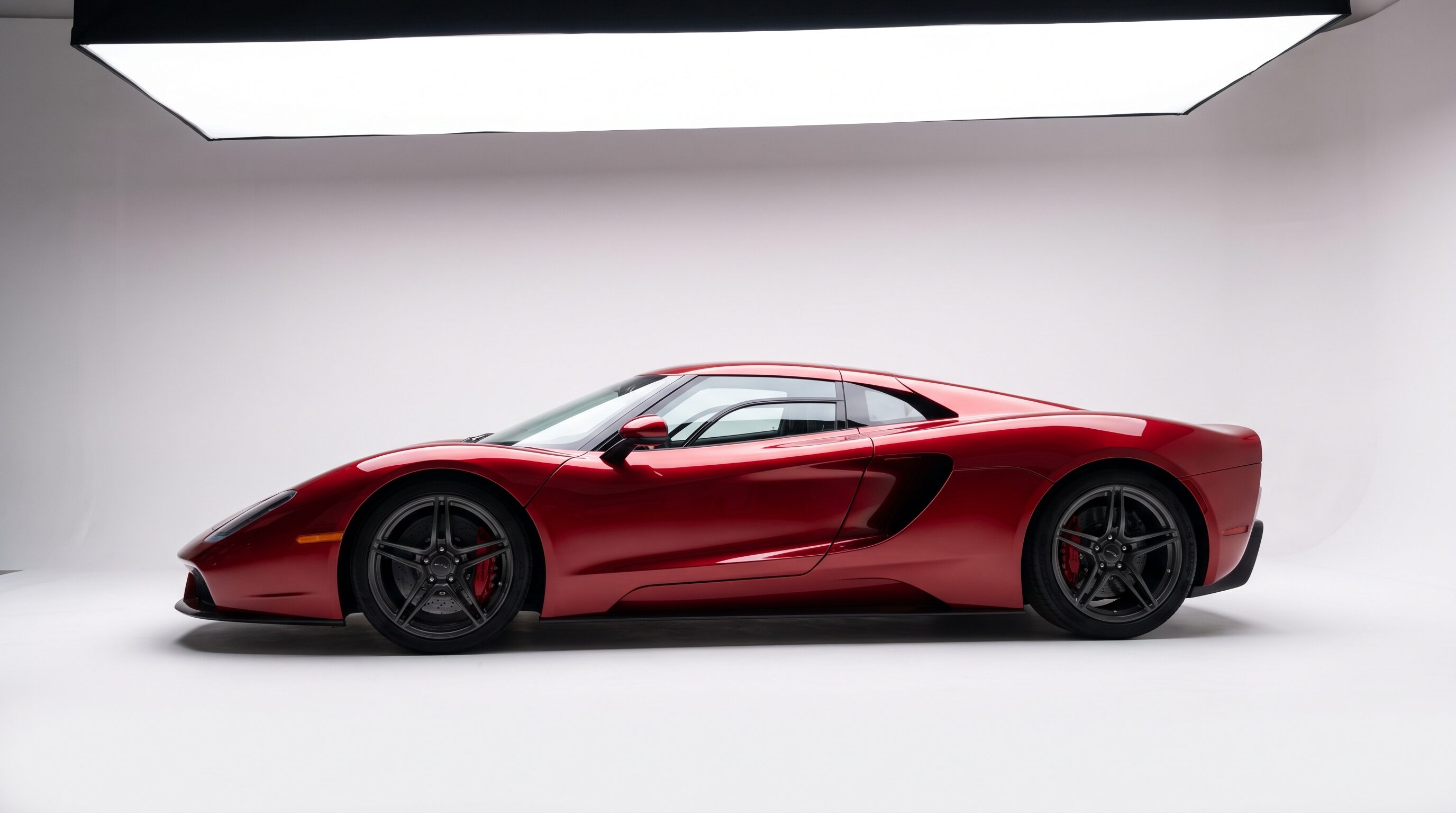 A deep red mid engine V12 supercar photographed on a white studio cyclorama