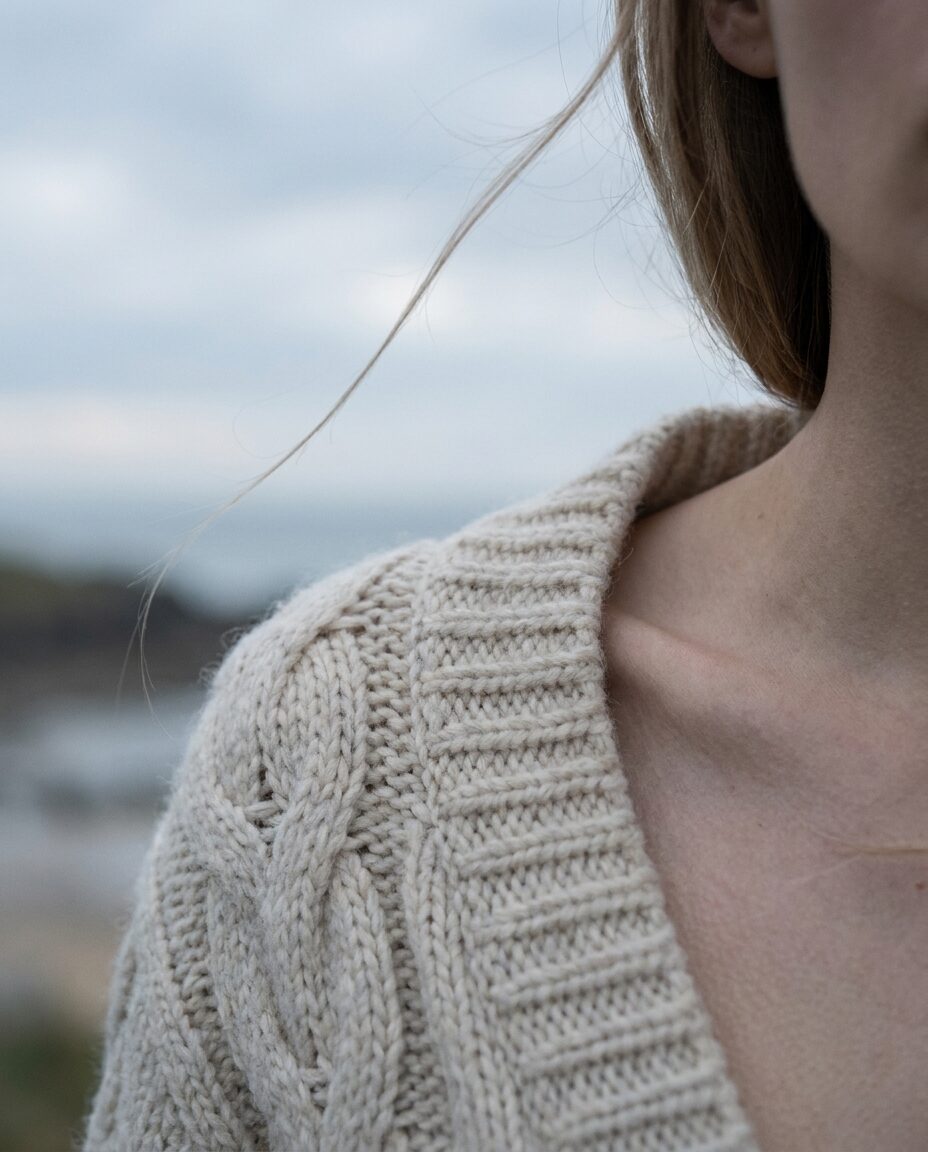 Close crop of cream wool texture at a model's shoulder, a strand of hair crossing the frame