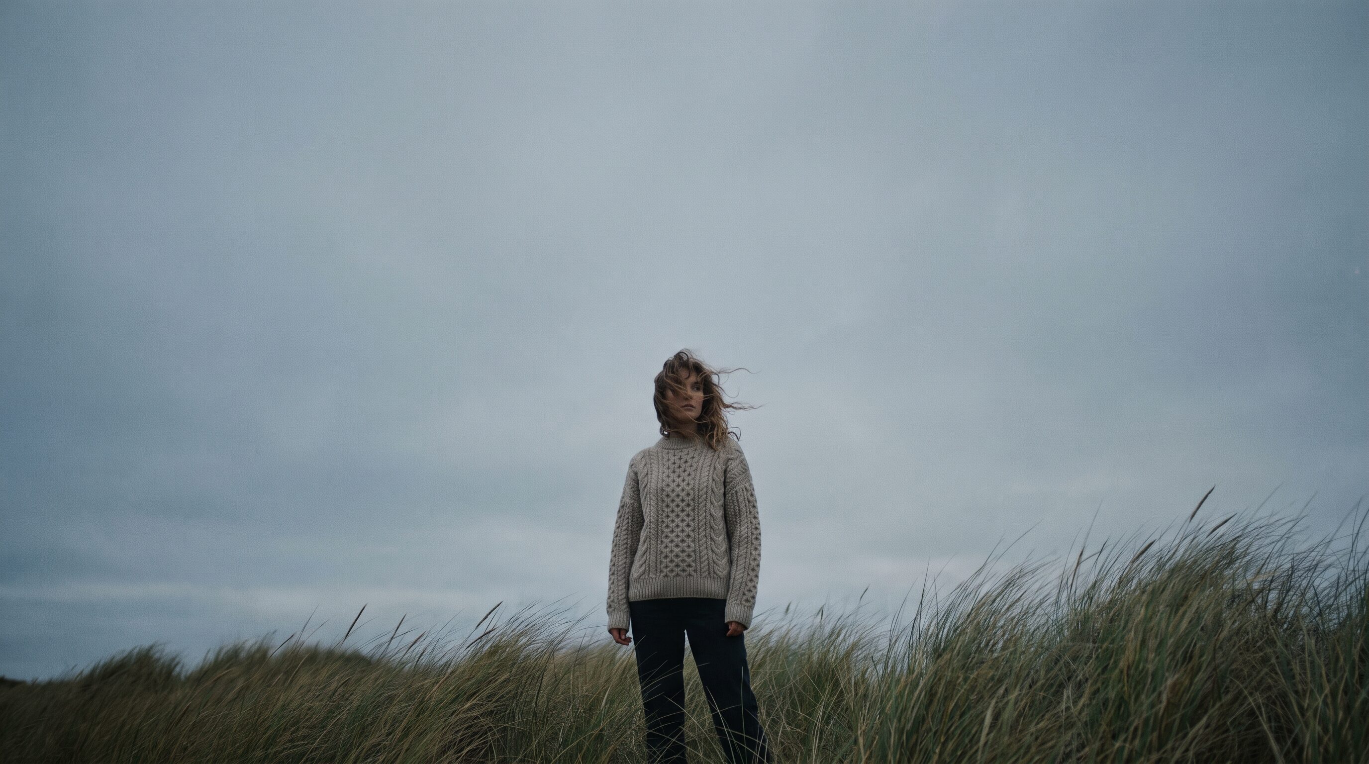 Model in an oatmeal jumper among windswept coastal dunes