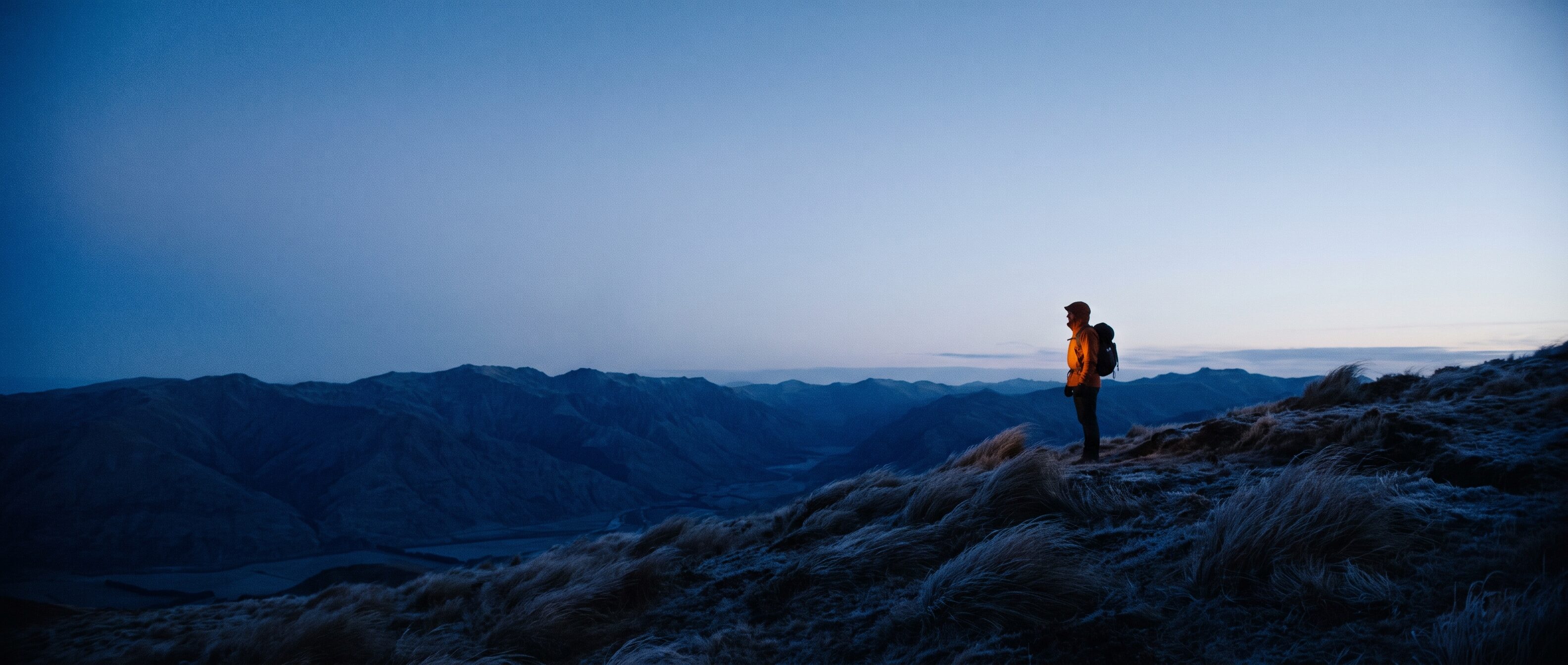 Hiker in an amber shell jacket on a blue-hour ridge