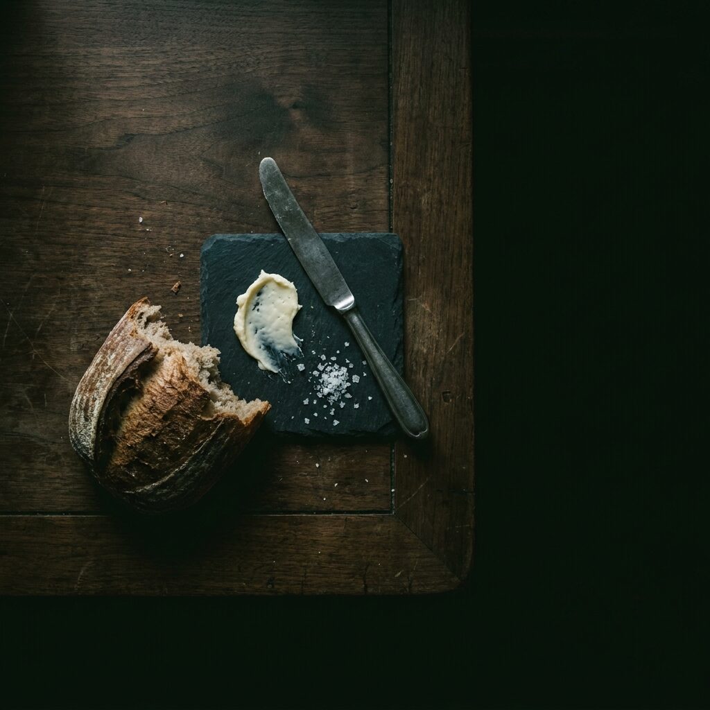 Overhead frame of torn sourdough, cultured butter and a pewter knife on walnut