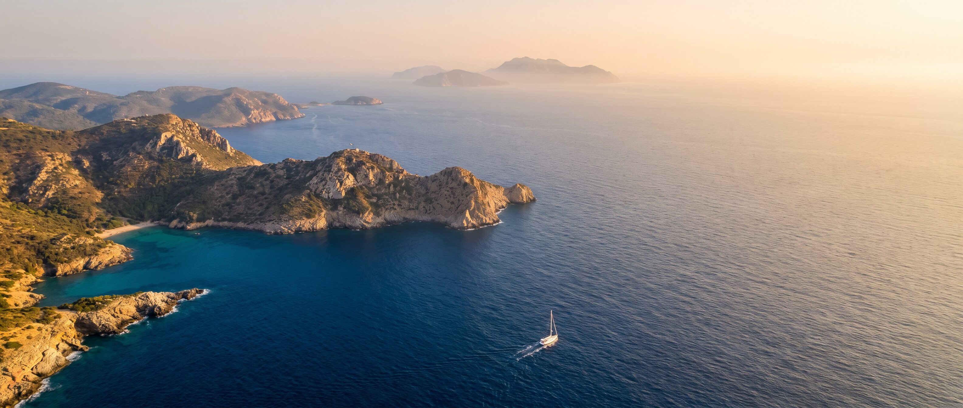 Aerial view of a Mediterranean coastline with a lone sailing yacht below